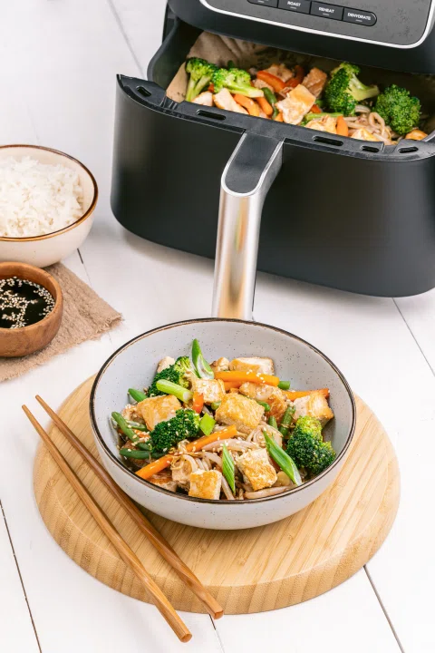 Air fryer con vegetales y bowl servido.