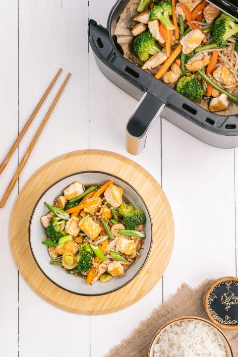 Air fryer con vegetales y plato servido.