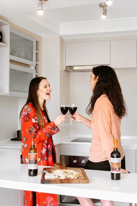 Dos mujeres comparten vino en una escena lifestyle de cocina.