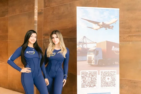 Dos anfitrionas posan junto a un stand promocional.