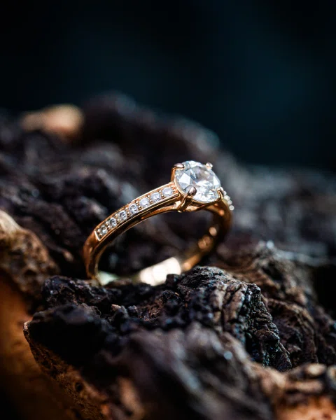Anillo dorado con piedra central fotografiado sobre una superficie de madera oscura.