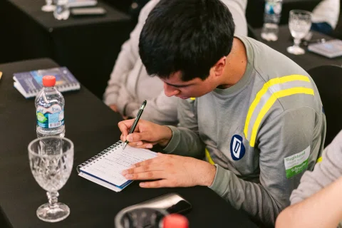 Asistente escribe en un cuaderno durante una presentación.