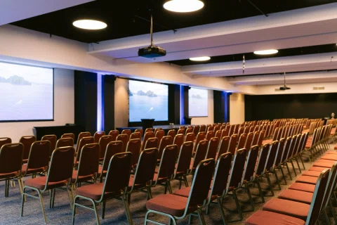 Auditorio vacío preparado con filas de sillas y pantallas.