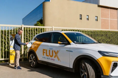 Automóvil carga energía en una estación identificada con Flux Solar Corp.