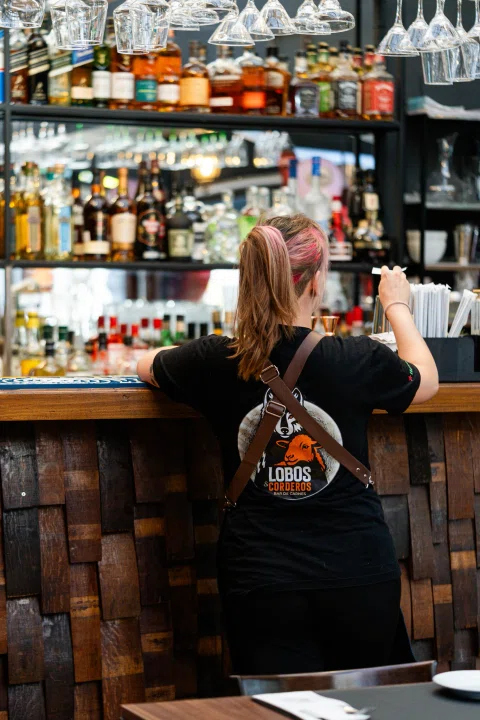 Bartender sentado frente a estantería de botellas.