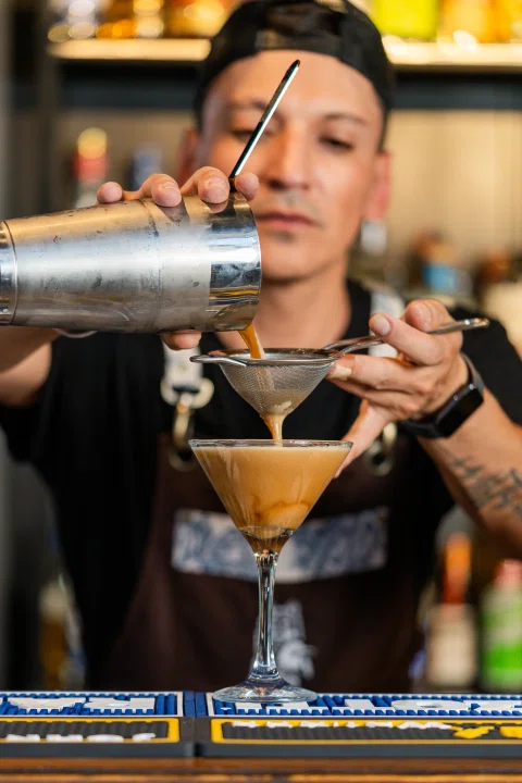 Bartender vertiendo cóctel amarillo en copa.