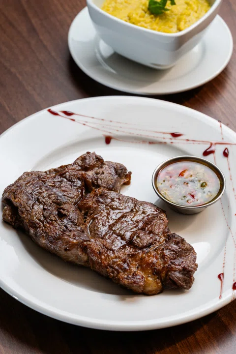 Bistec a la parrilla servido con salsa y acompañamiento.