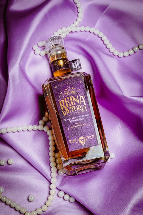 Botella de licor sobre satín morado y elementos decorativos.