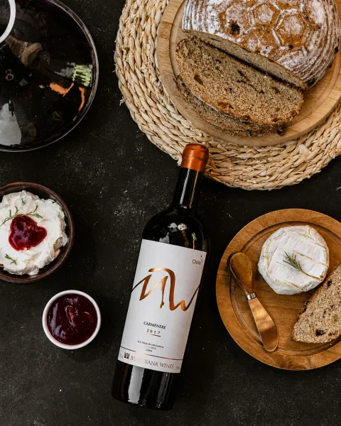 Botella de vino blanco en mesa con panes y quesos.