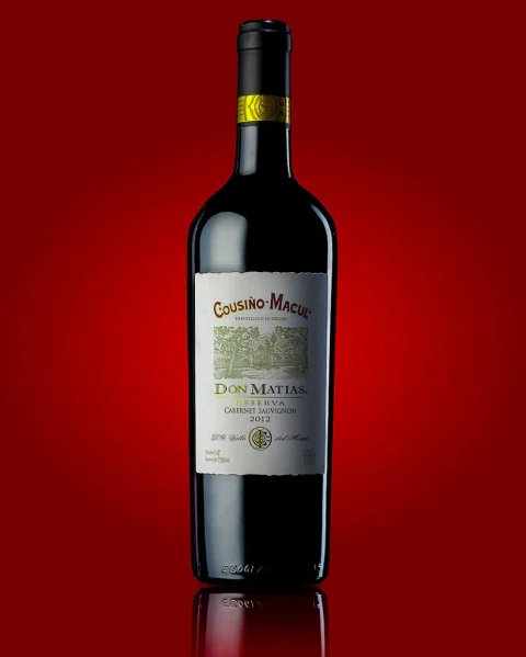 Botella de vino fotografiada sobre una superficie reflectante con fondo rojo.