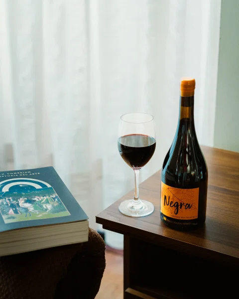Botella de vino naranja junto a copa y libro.