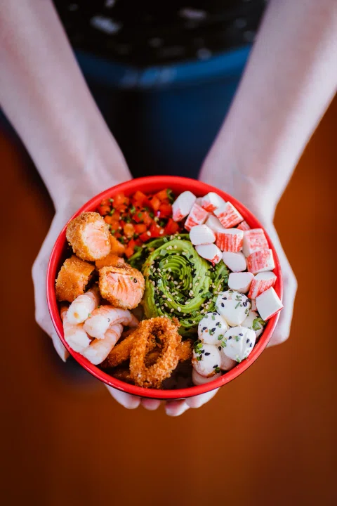 Bowl de poke con distintos ingredientes sostenido entre dos manos.