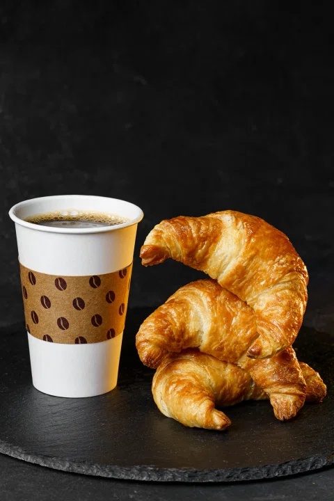 Café para llevar acompañado de croissants sobre una bandeja negra.
