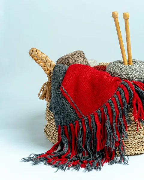 Canasto con ovillos y manta roja tejida.