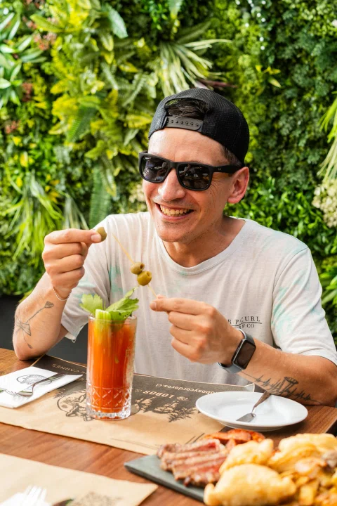 Cliente con gafas sosteniendo cerveza en terraza.
