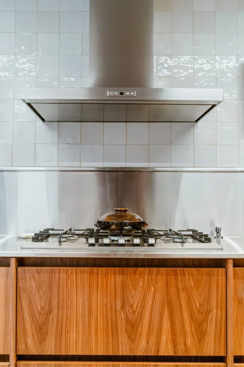 Detalle de cocina con encimera a gas, cubierta de madera y campana de acero.