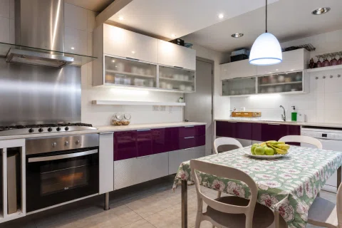 Cocina residencial amplia con mobiliario blanco, mesa central y equipamiento de acero.