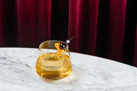 Cóctel ámbar en vaso bajo sobre mesa de mármol.
