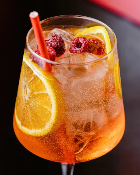 Cóctel naranja con frutos rojos y rodaja de limón.