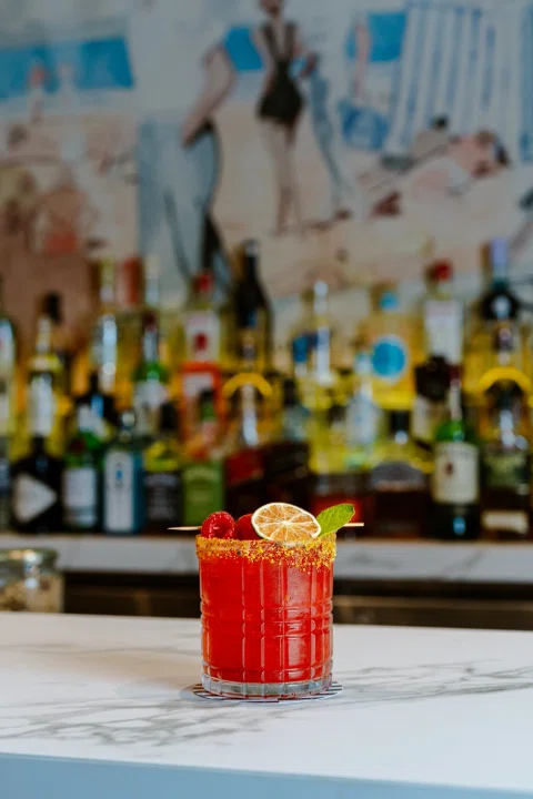 Cóctel rojo sobre barra frente a botellas.