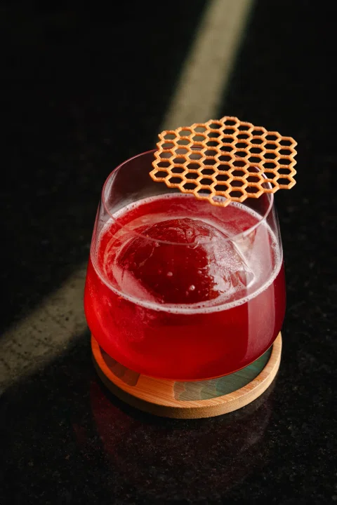 Cóctel rojo con hielo y decoración geométrica sobre una mesa oscura.