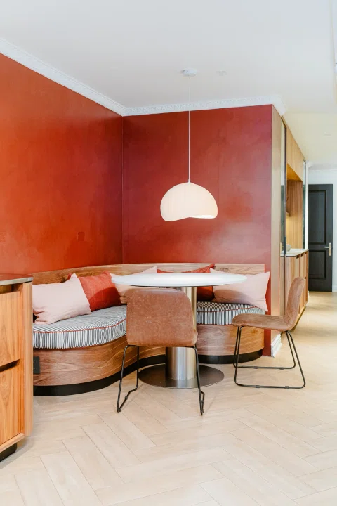 Comedor de hotel con banca curva y pared roja.