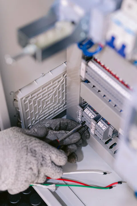 Técnico con guante realiza una conexión de cables dentro de un tablero eléctrico.