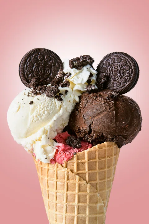Cono de helado con galletas y crema sobre fondo rosado.