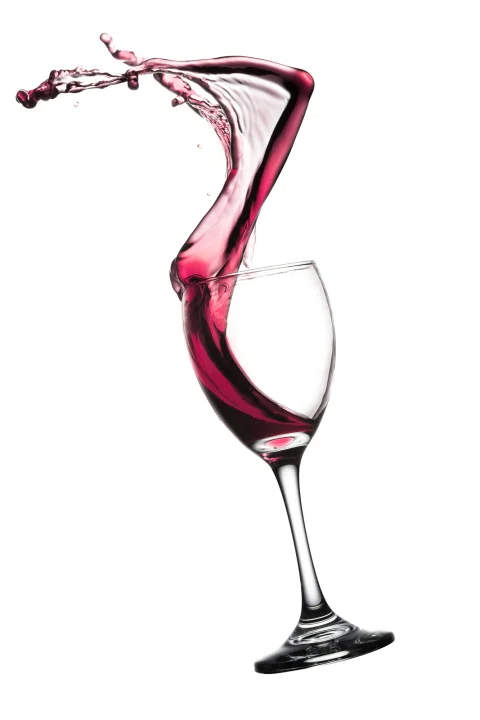 Copa con vino tinto y salpicadura suspendida sobre fondo blanco.