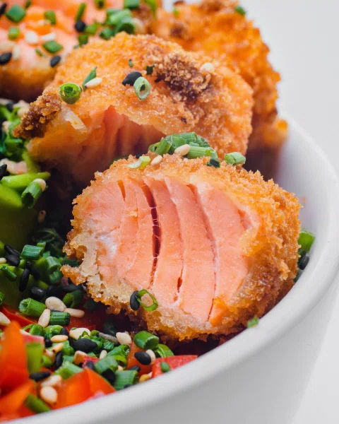 Corte de salmón sellado sobre arroz y vegetales.