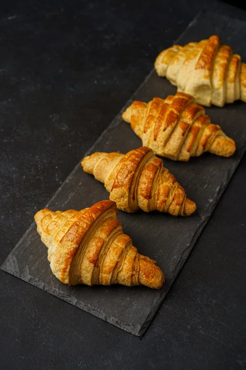 Croissants horneados alineados sobre una bandeja negra.