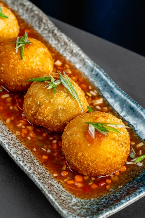 Croquetas doradas con salsa en plato rectangular.