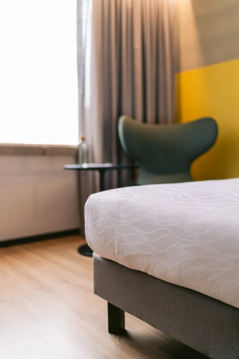 Detalle de cama y sillón verde en habitación.