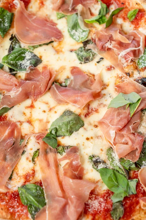 Detalle de pizza con jamón queso tomate y hojas verdes.