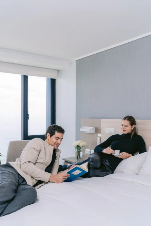 Dos hombres conversando sobre cama de hotel.