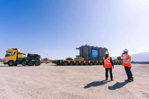 Dos trabajadores frente a transformador y camiones en desierto.