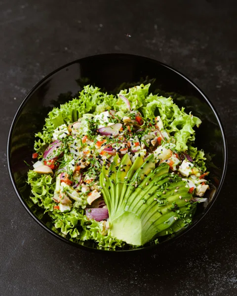 Ensalada verde con palta y proteína en bowl negro.