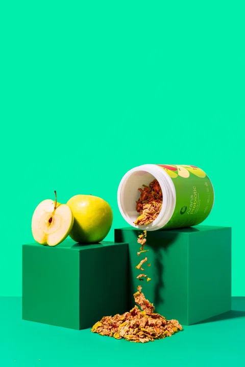 Envase verde con manzana y producto derramado en un bodegón de tonos verdes.