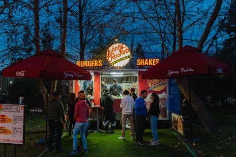 Personas frente a un puesto de hamburguesas durante una feria gastronómica nocturna.