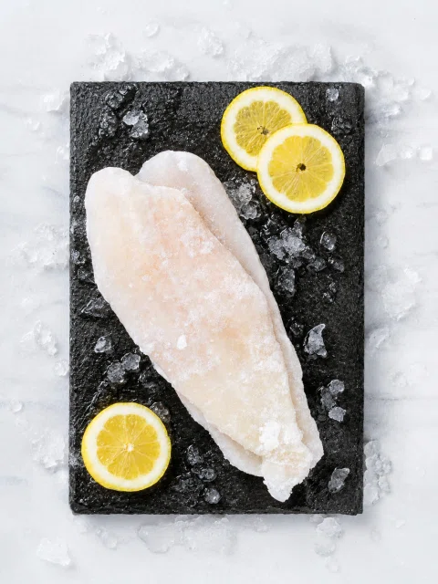 Filete de pescado blanco sobre pizarra con limón.