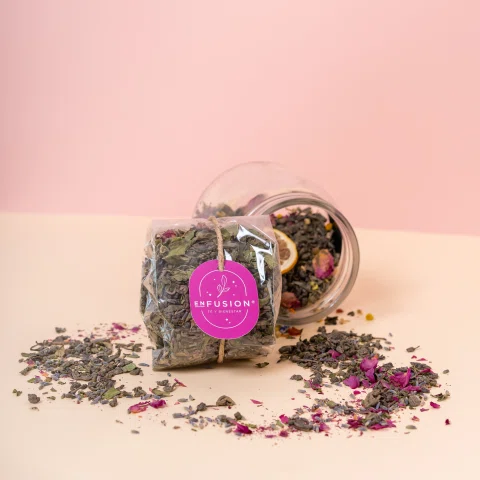 Frasco de infusión rosada volcado con hierbas y flores.