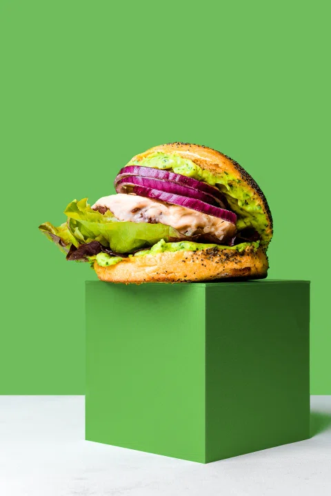 Hamburguesa de pan verde presentada sobre un bloque de color.