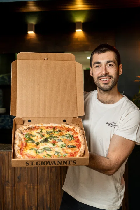 Hombre mostrando pizza dentro de caja St Giovanni's.