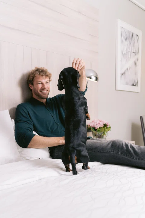 Hombre sentado en cama acariciando perro negro.