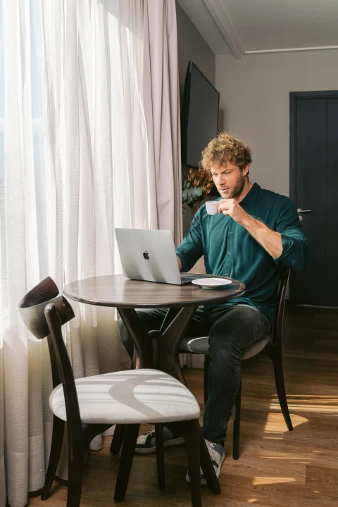 Hombre sentado en mesa de habitación tomando bebida.