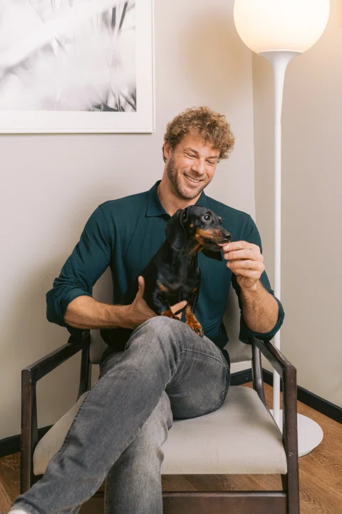 Hombre sentado sosteniendo perro negro en habitación.