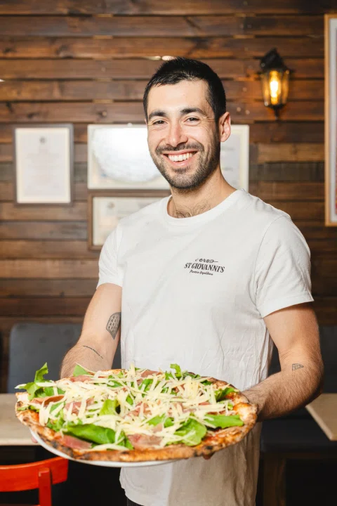 Hombre sosteniendo pizza con hojas verdes.