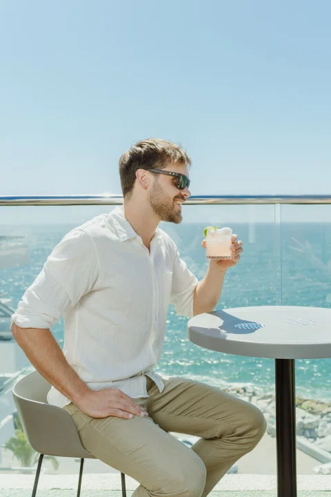 Hombre tomando bebida en mesa de terraza.