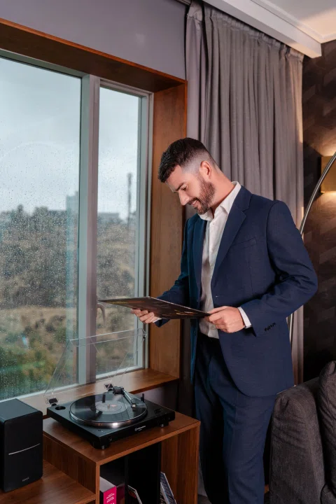 Hombre de traje preparando bebida junto a ventana.