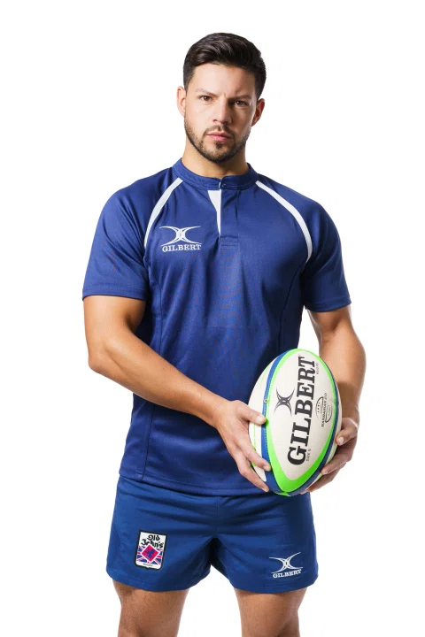Jugador de rugby con uniforme azul sostiene un balón sobre fondo blanco.